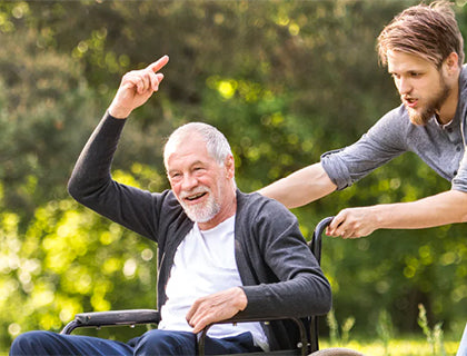 An elderly man being pushed by a caregiver