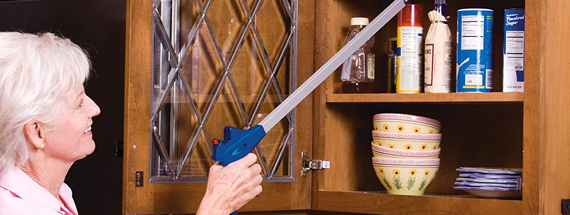 An elderly woman using a reacher grabber to obtain an item in her cabinet