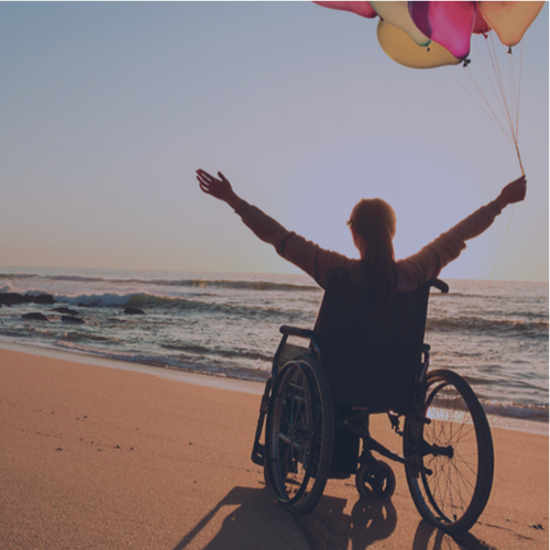 A person in a wheelchair holding balloons on a beach