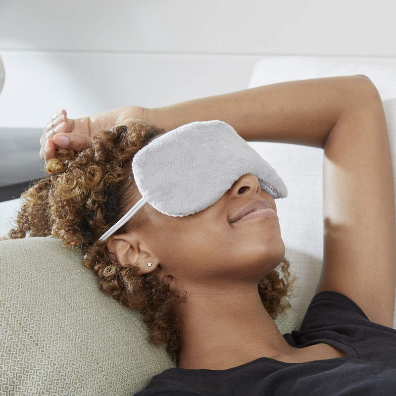 A smiling woman lying on a couch with the Carex Lavender Eye Mask over her eyes