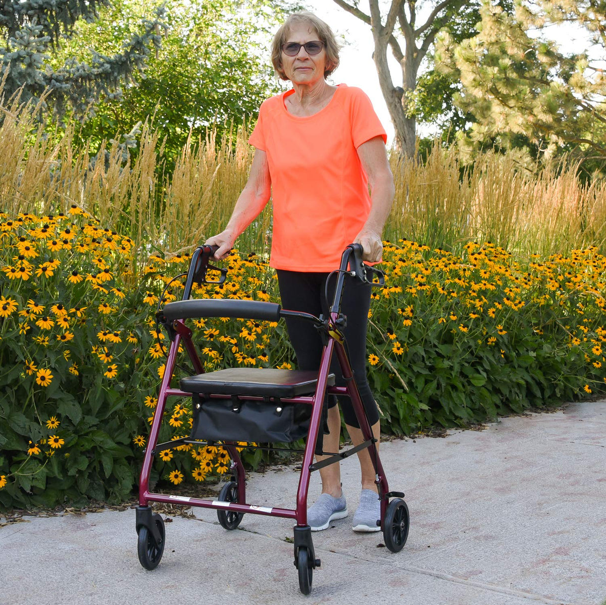 An elderly woman walking with the ProBasics Aluminum Rollator in a park