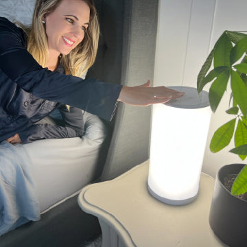 A woman turning a therapy lamp on next to her bed