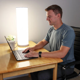 A man working on a laptop next to the 24” Bright Health therapy lamp