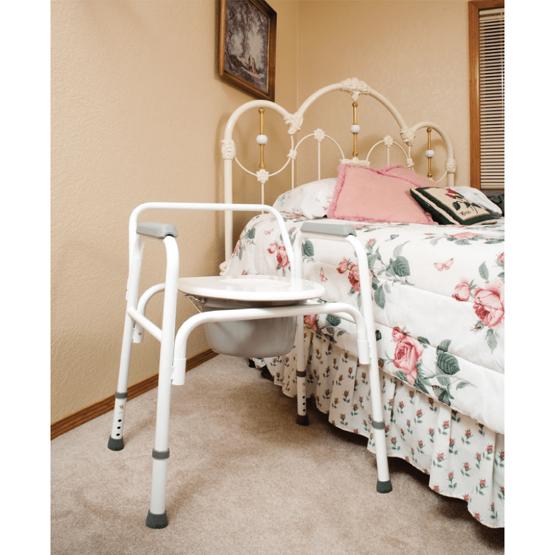 The Carex Bedside Steel Commode sitting next to a bed