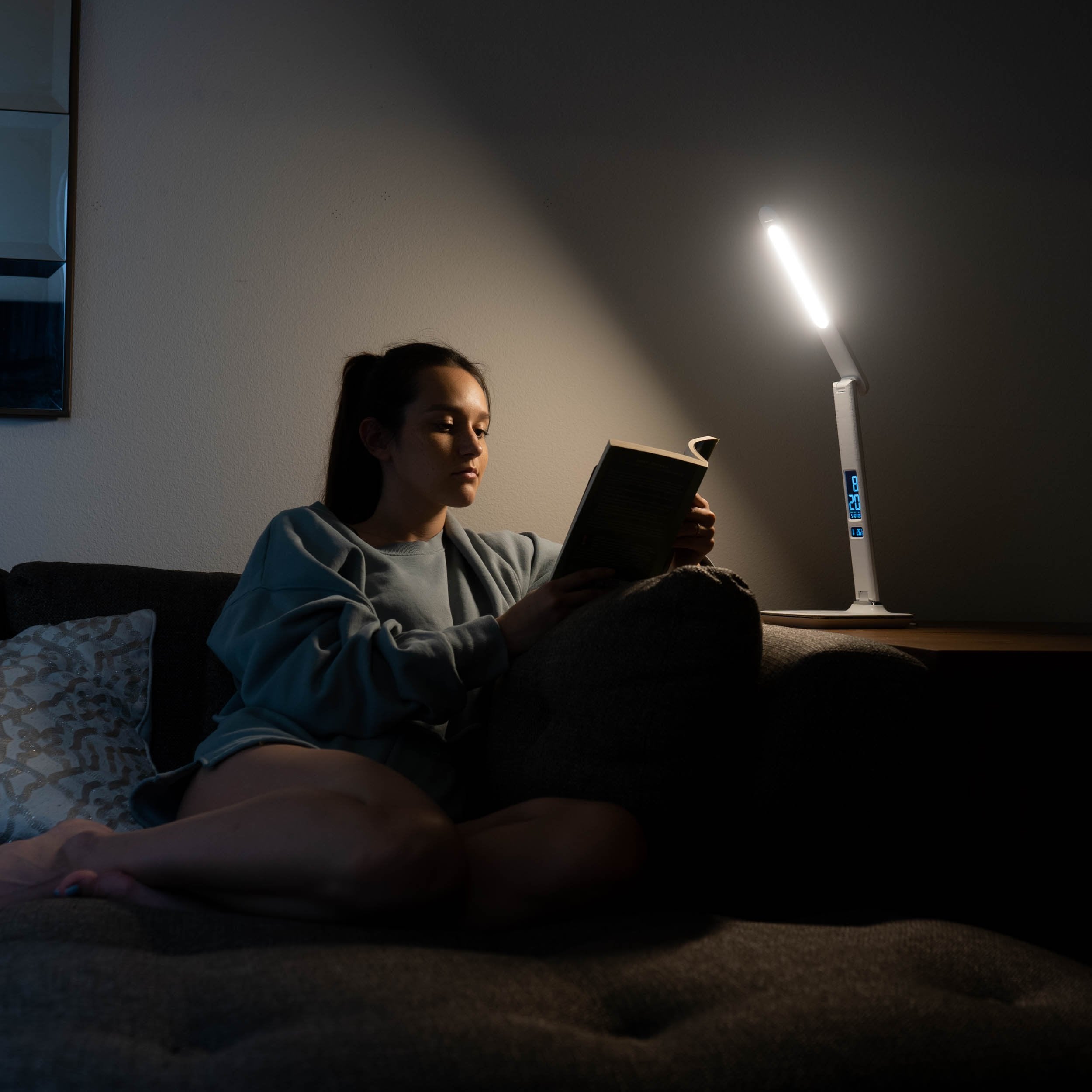 A woman reading a book while sitting under a therapy lamp
