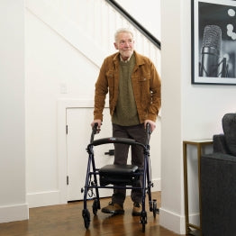 A man walking around a corner inside with the Carex Steel Rolling Walker