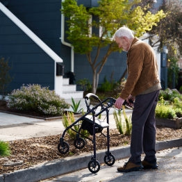 A man using the Carex Steel Rolling Walker to step over a curb