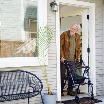 A man stepping outside his house with the Carex Steel Rolling Walker 