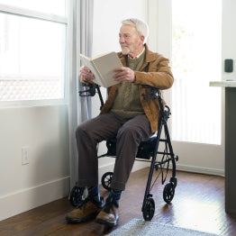 A man sitting on the Carex Steel Rolling Walker reading a book