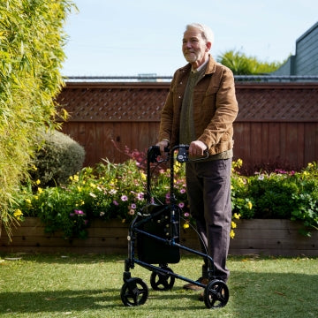 A man standing with hands on the Carex Trio Rollator outside on grass