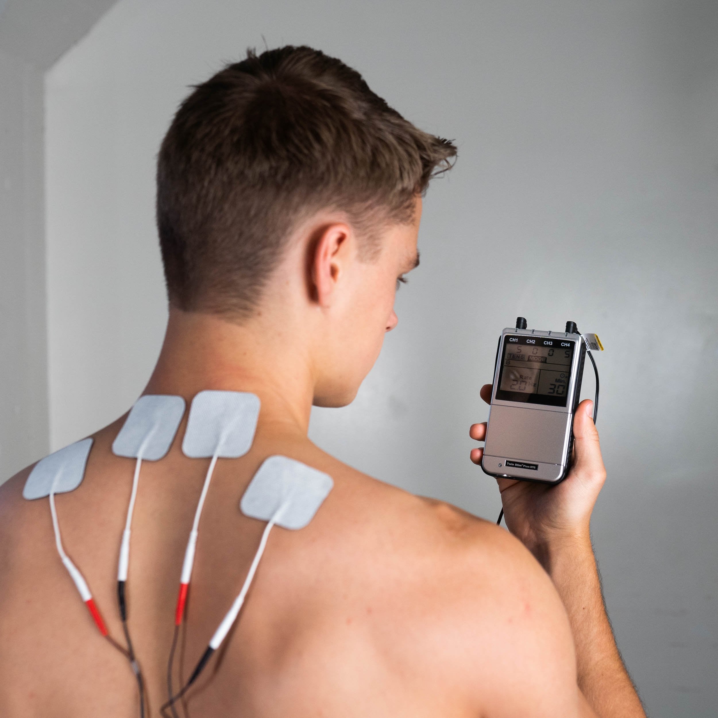 A man holding a TENS unit with electrodes on his upper back