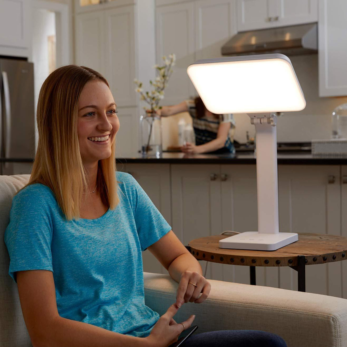 Woman sitting on a couch in front of the TheraLite Aura light therapy lamp