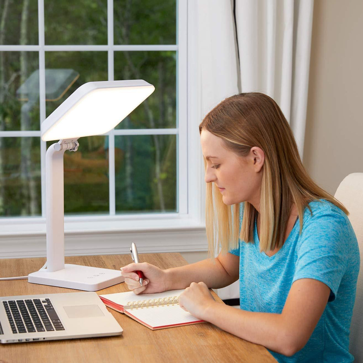 A woman writing next to a therapy lamp