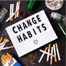 A sign saying “Change Habits” surrounded by cigarettes and alcohol bottles