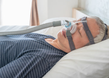 A man sleeping on his back in bed with a CPAP mask on