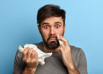 A man with red eyes, a tissue, and nose medicine