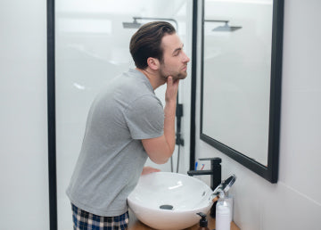 A man in a mirror looking at his facial hair