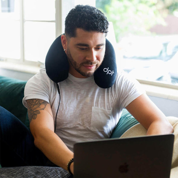 A man sitting down working on a laptop with the DPL Red Light Therapy Neck Pillow on his neck