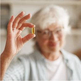 An elderly woman holding up a pill