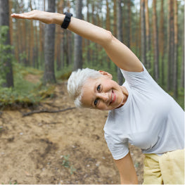 An elderly woman stretching in woods