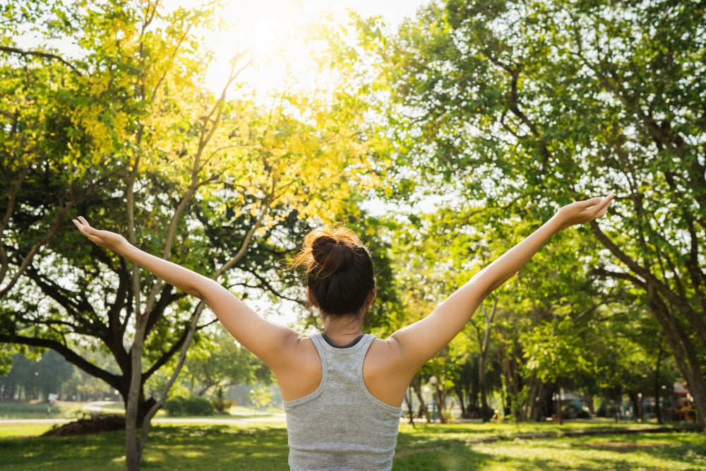 A woman spreading her arms in a forest in front of sunlight