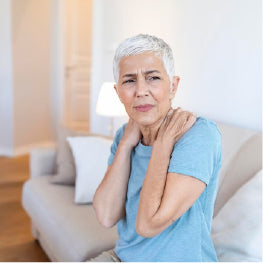 An elderly woman holding her shoulders in pain