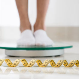 A close up of feet on a weight scale in front of measuring tape