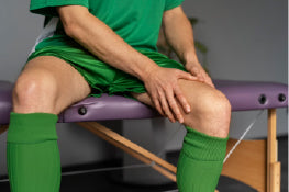 A soccer player sitting on a doctor’s table holding his thigh in pain