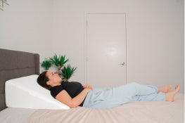 A woman laying in bed using a wedge pillow to prop her back up