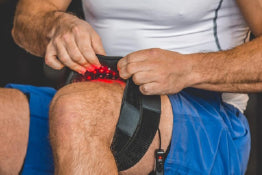 A man adjusting a red light therapy device on his thigh