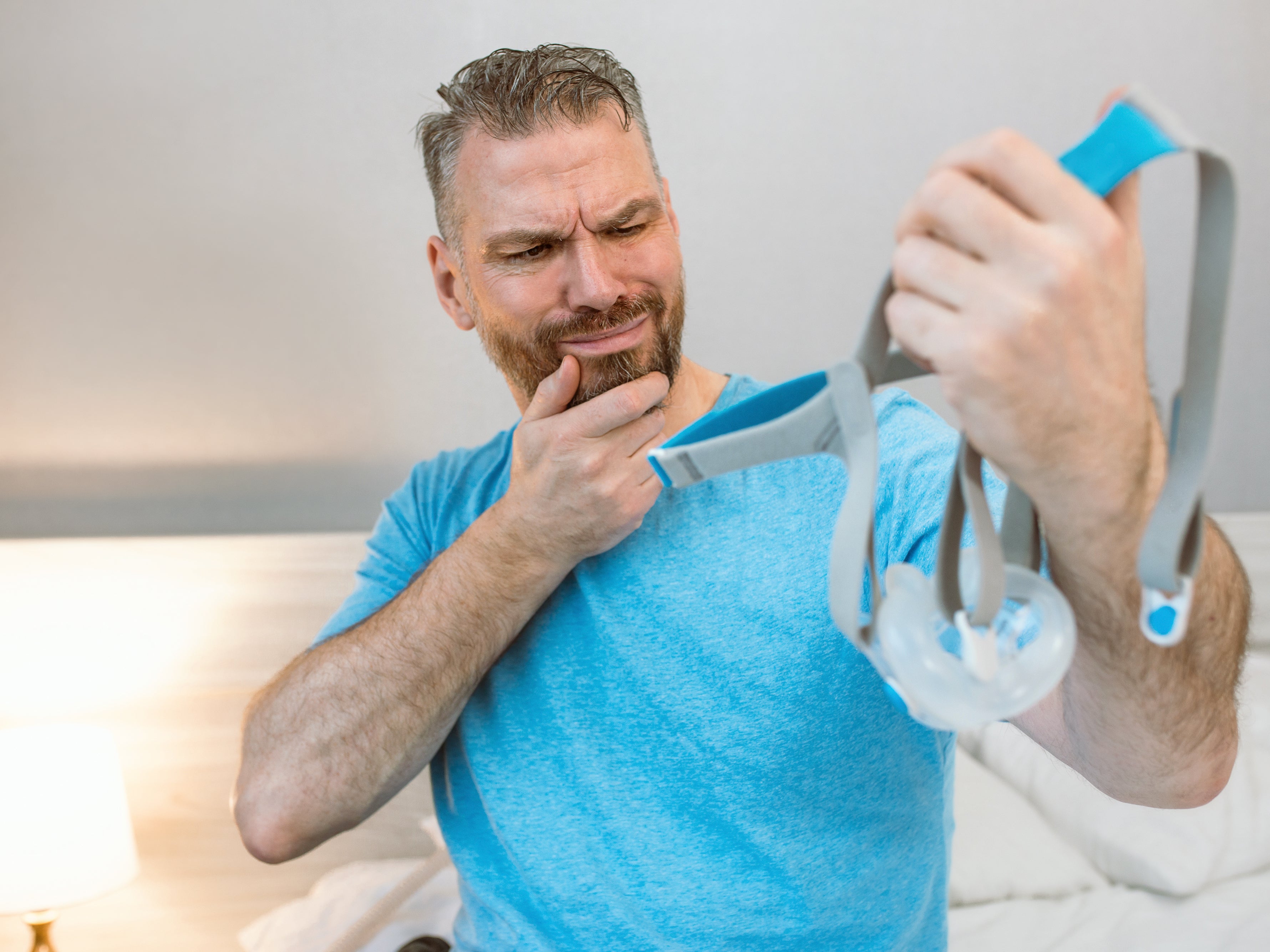 A man looking at his CPAP mask in confusion