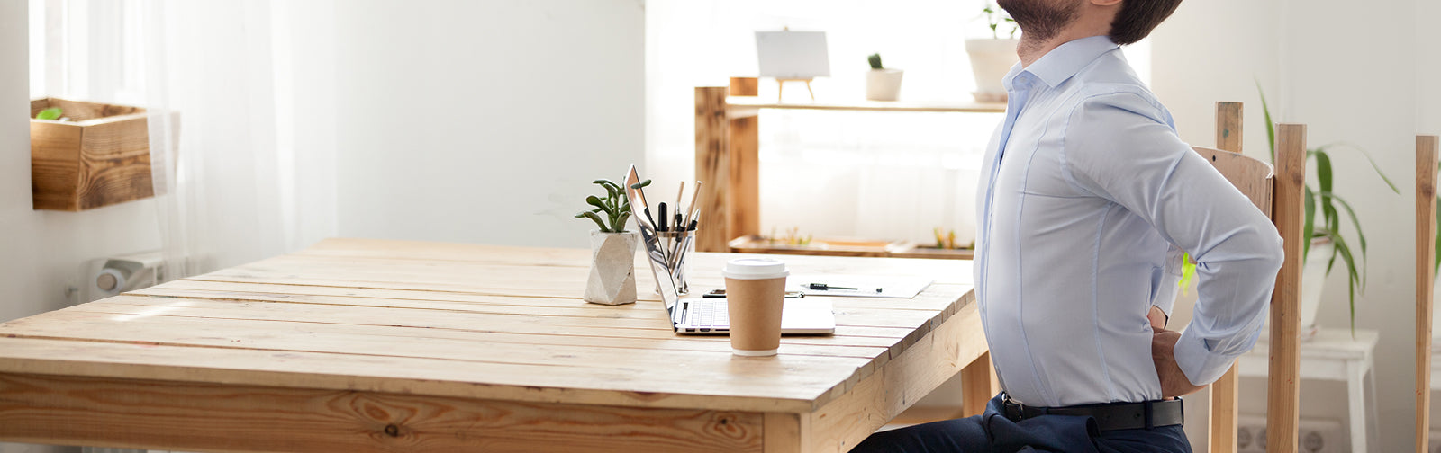 A man sitting at a table holding his lower back in pain