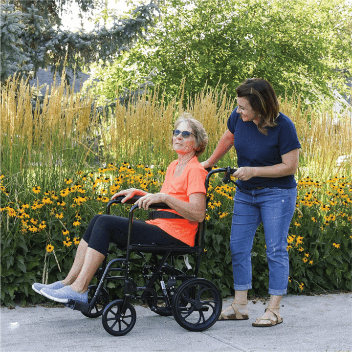 An elderly woman sitting in the ProBasics Aluminum Transport Chair being pushed by a caregiver