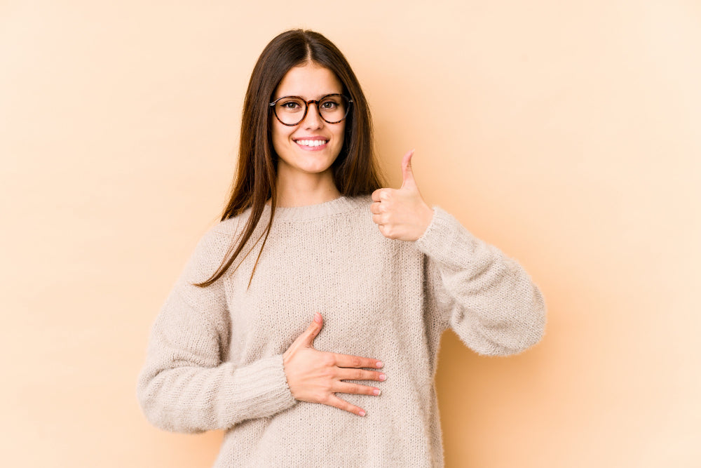 A woman holding her stomach gesturing with a thumbs 