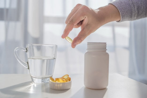 A person holding a vitamin D capsule next to a class of water