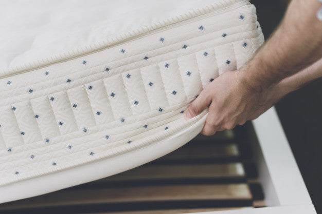 A mans hands lifting up a mattress