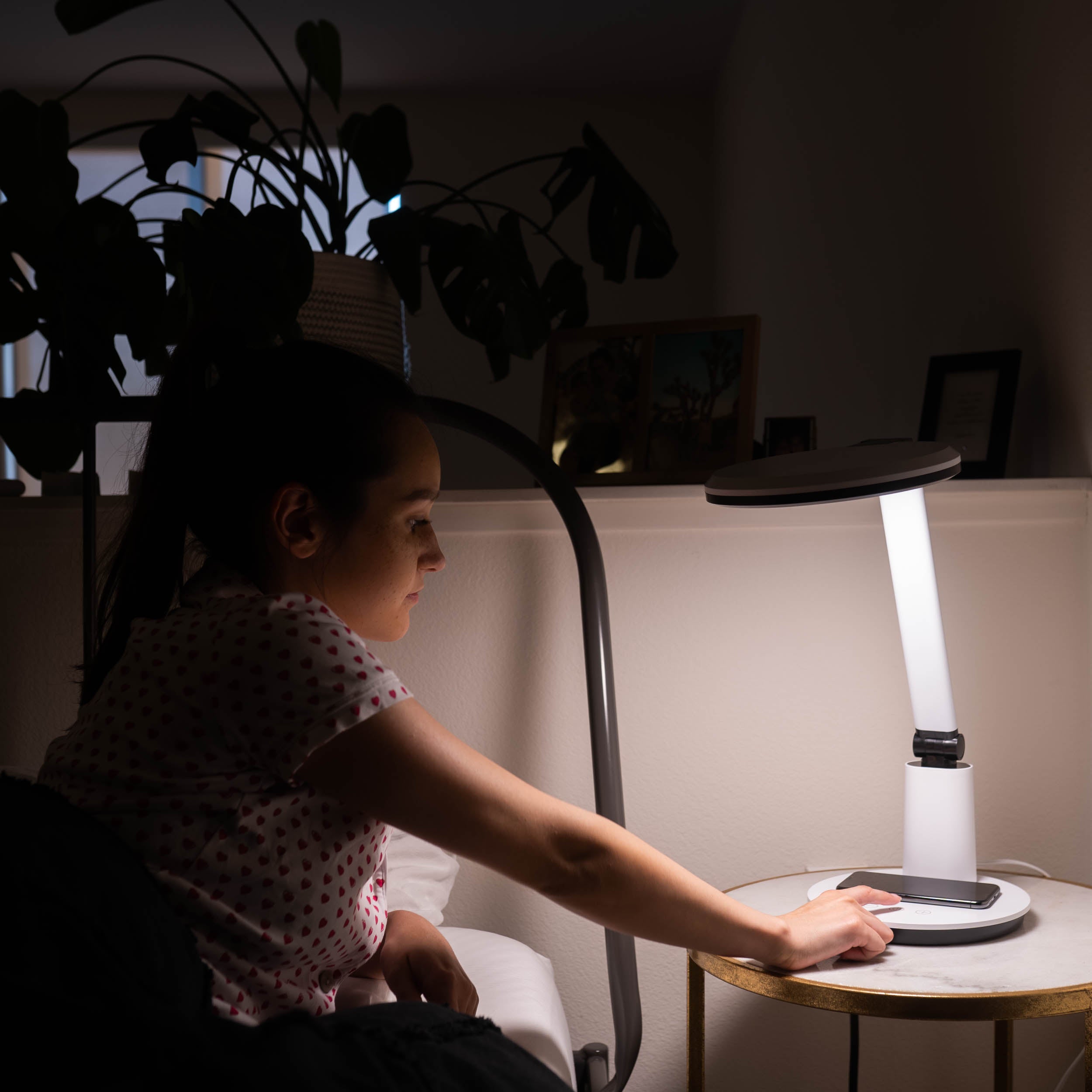 A woman turning a therapy lamp on next to her bed