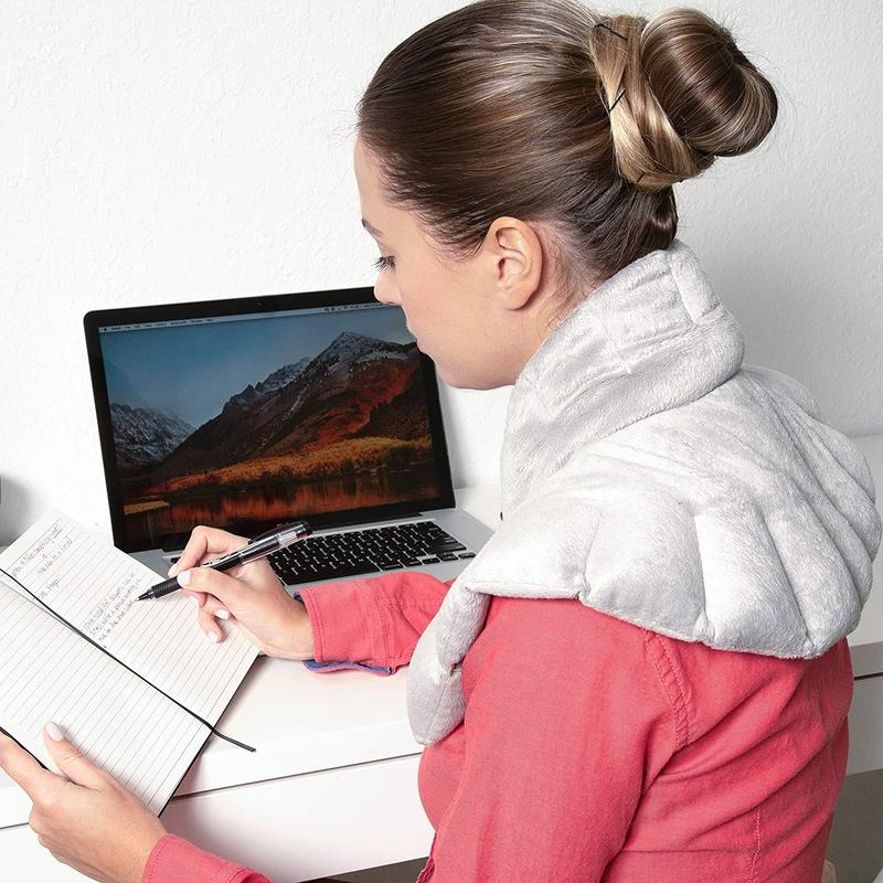 A woman with the Bed Buddy wrap over her shoulders while writing at a desk