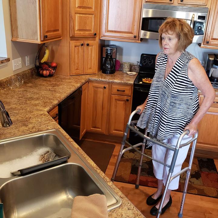 An elderly woman using the Carex Folding Walker in a kitchen