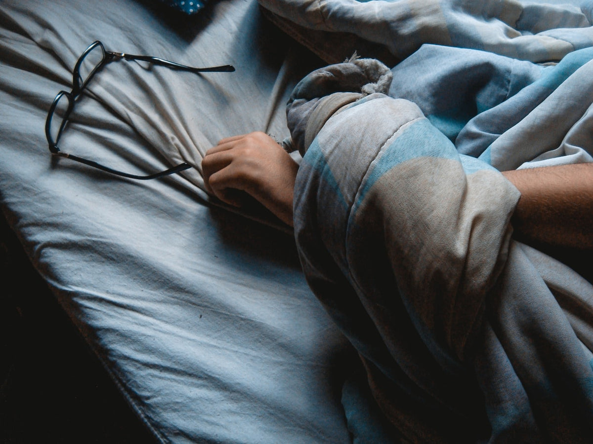 A person's hand asleep on a bed next to glasses