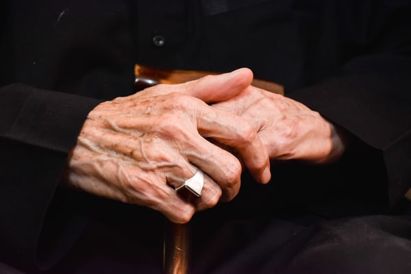 An elderly womans hands holding a wooden walking cane