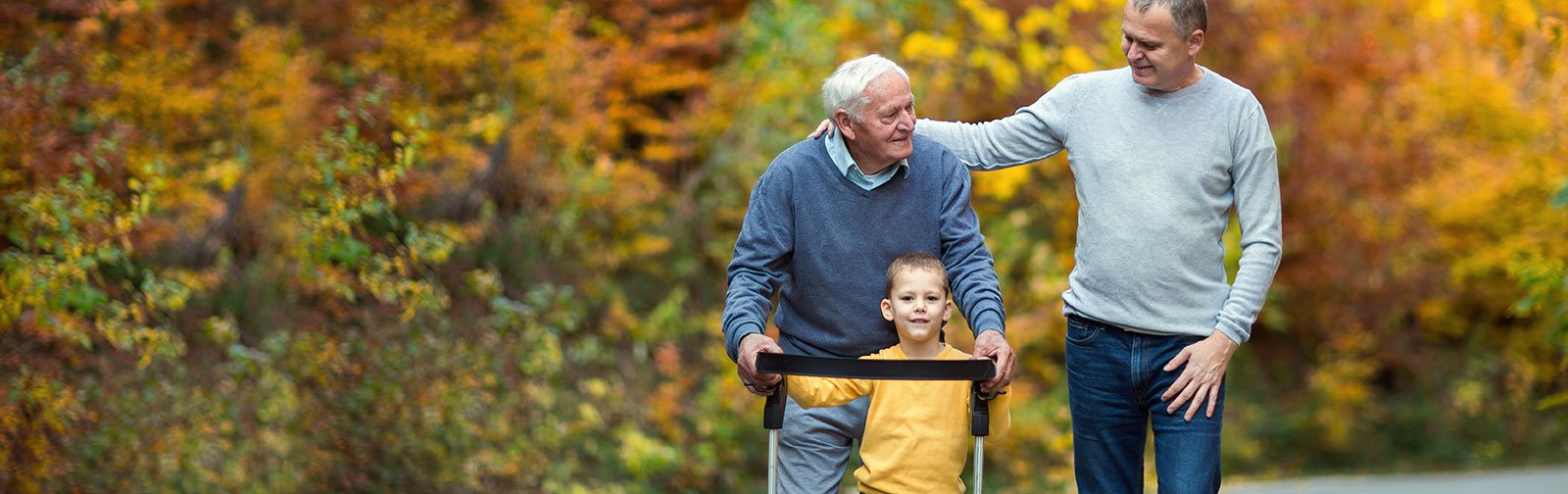 An elderly man using a walker with his son and grandchild