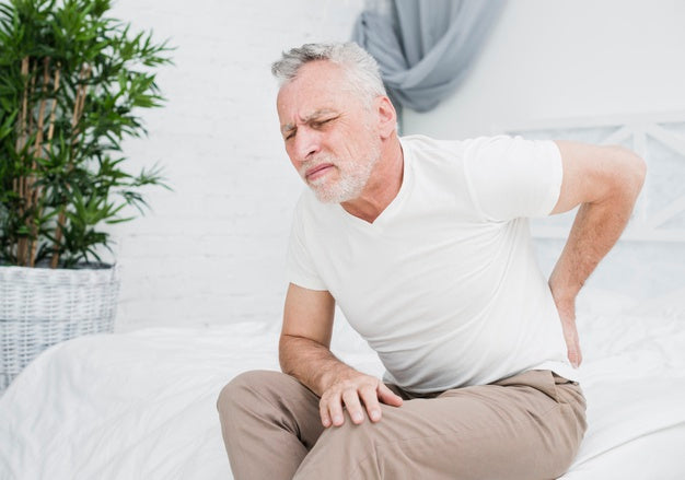 A man sitting on a bed holding his back in pain