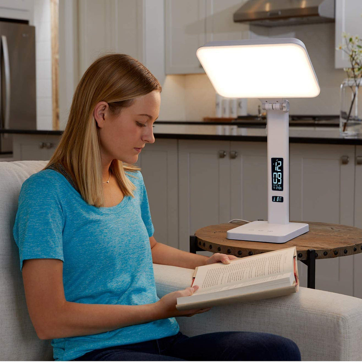 A woman reading on a couch next to a therapy lamp