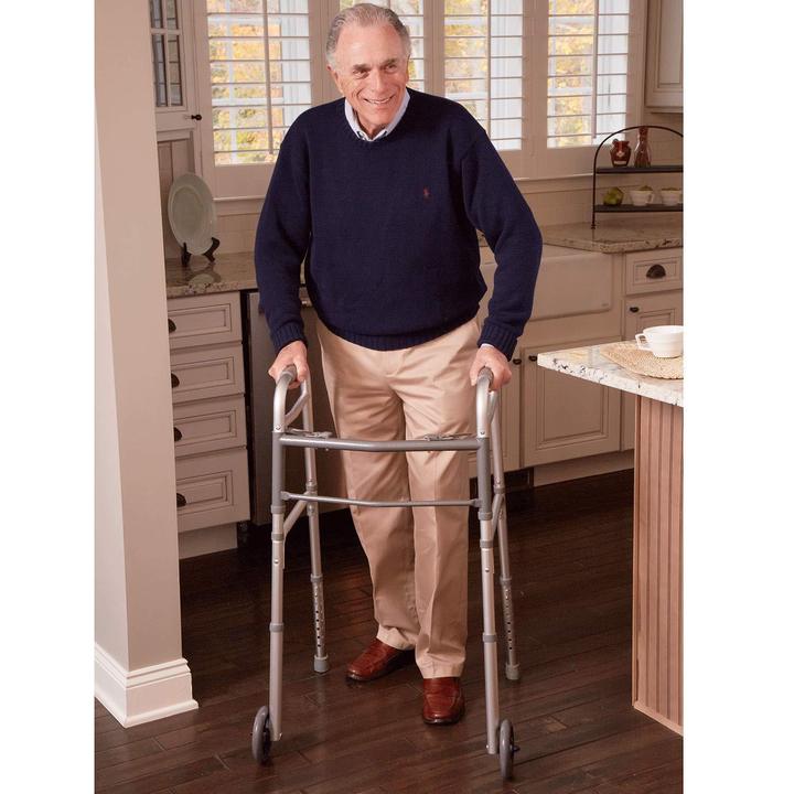 An elderly man using the Carex Folding Walker in a kitchen