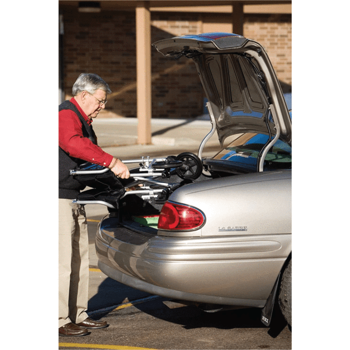 An elderly man placing the folded Pro Basics Steel Transport Chair into his car trunk