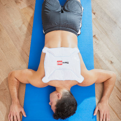 A man on his stomach using a hot/cold wrap on his upper back