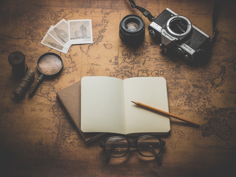 A travel journal over a map next to various items for traveling