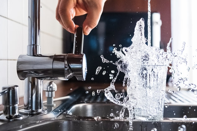 A person turning a faucet on with water spilling out of a glass