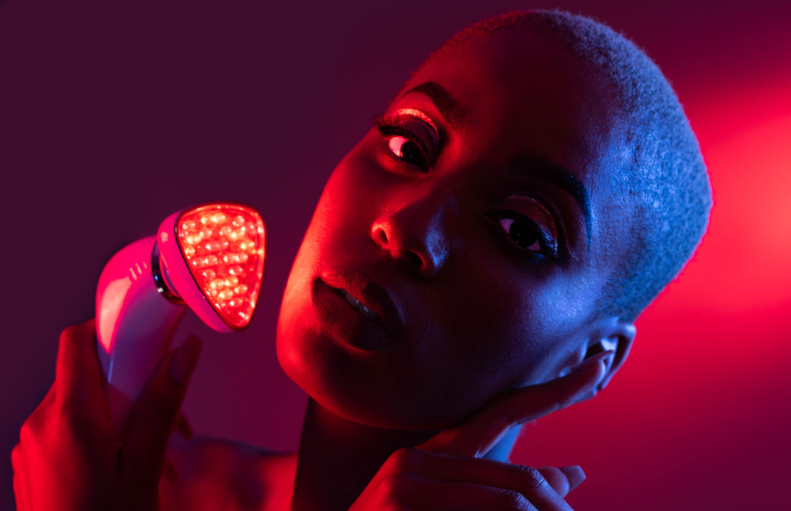 A woman holding a red light therapy device on her face